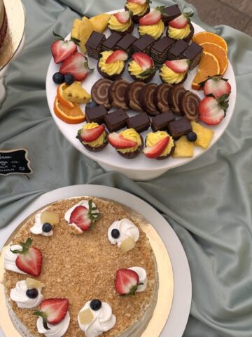 Sitni kolači bajadera, rolati i voćne korpice poređani na stalcima i dekorisani voćem